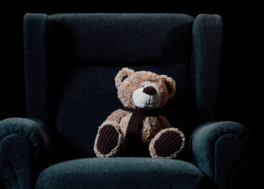 beige teddy bear in grey soft armchair isolated on black